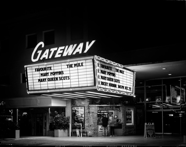 A movie theater marquee with neon lights advertises several films at night.
