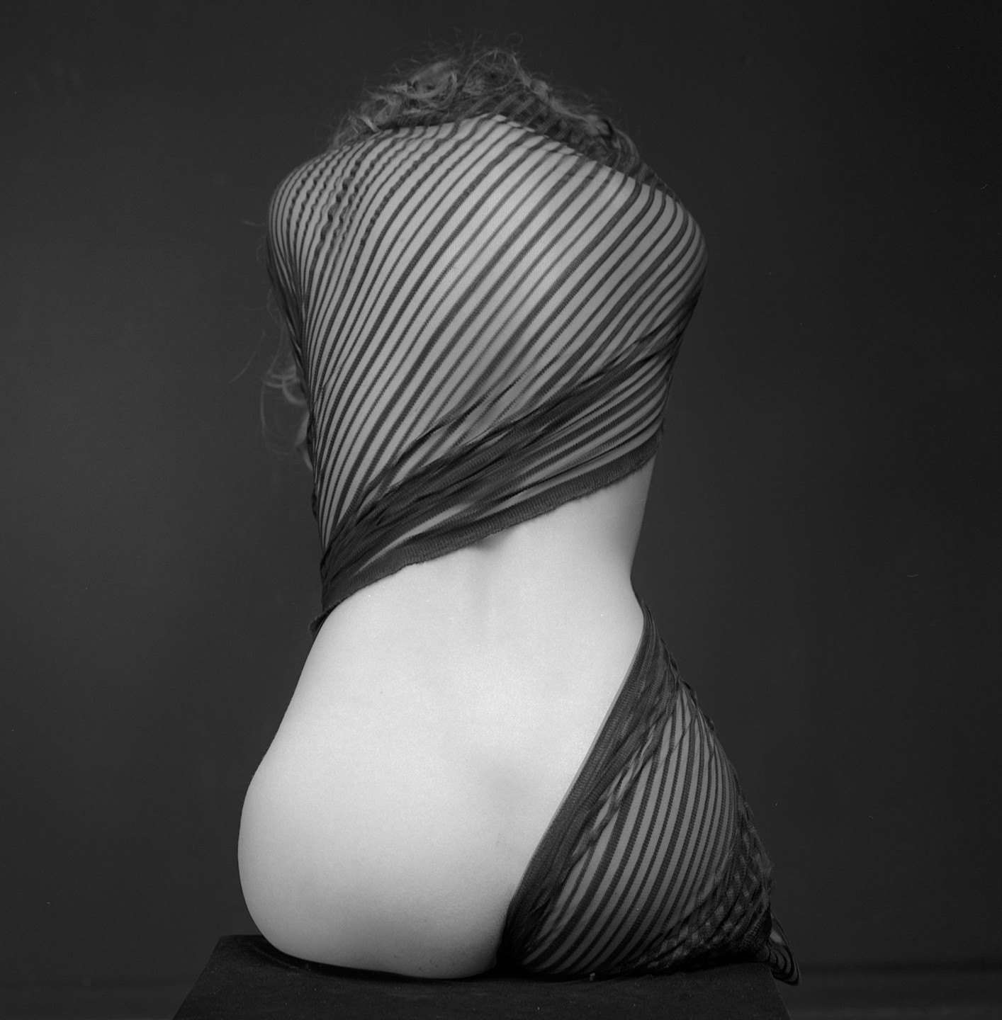 A woman's back is visible, partially covered by a striped sheer fabric.