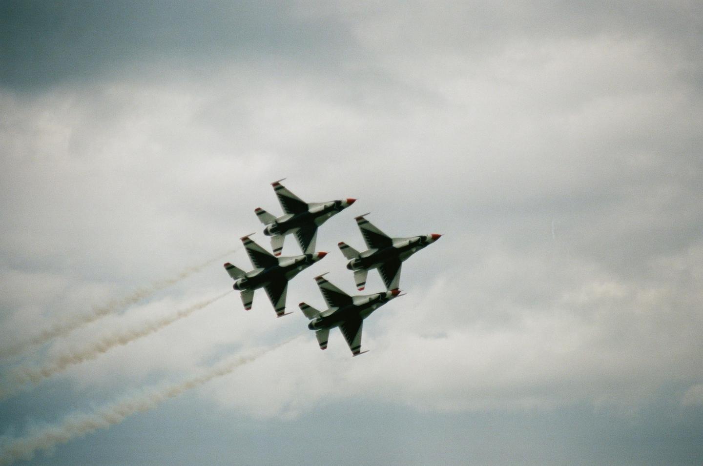 Four fighter jets fly in formation against a cloudy sky, leaving smoke trails behind them.