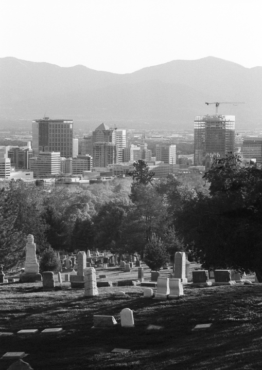 A cemetery with many gravestones is in the foreground, with a city skyline and mountains in the background.