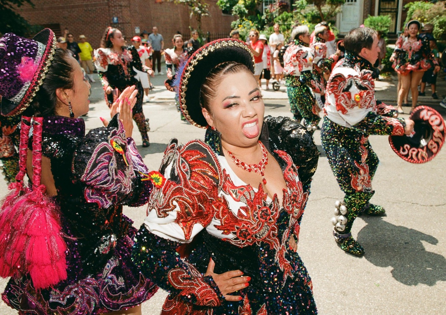 A woman in a sequined dress and hat makes a face at the camera while dancing in a parade.