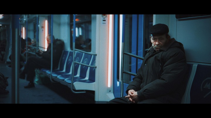 A man in a dark coat and hat sits on a subway train.
