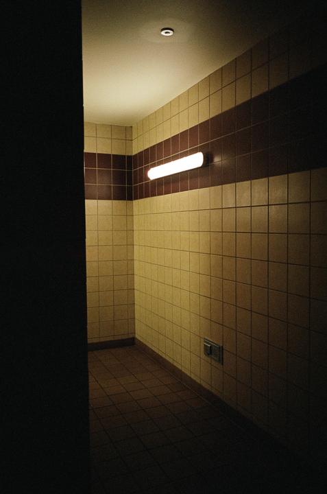 A fluorescent light illuminates a tiled room with a dark brown stripe.
