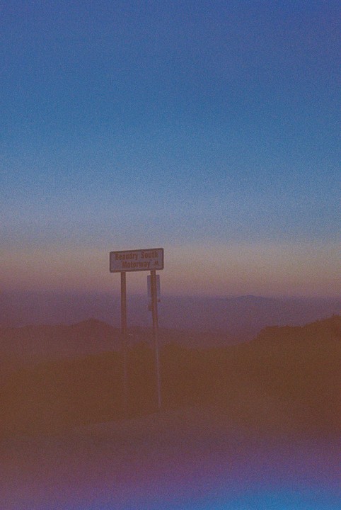 A road sign for Beaudry South Motorway stands on a hill overlooking a hazy landscape at dusk.