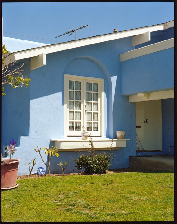 A light blue house with a white window and a green lawn in front.