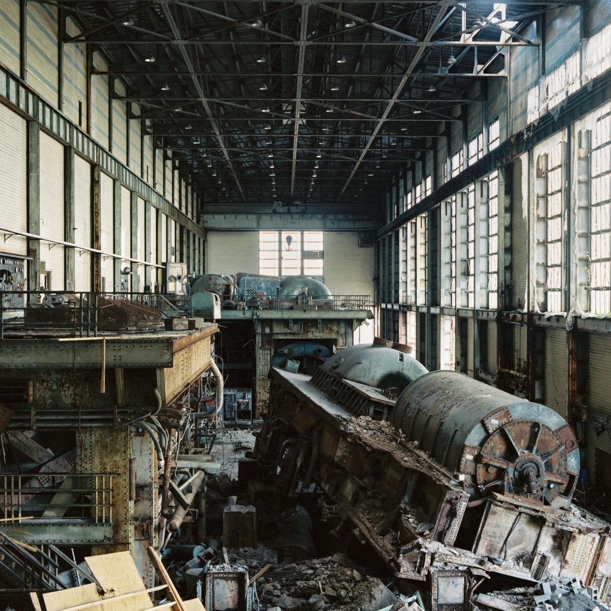 A large, abandoned industrial building is filled with decaying machinery and debris.