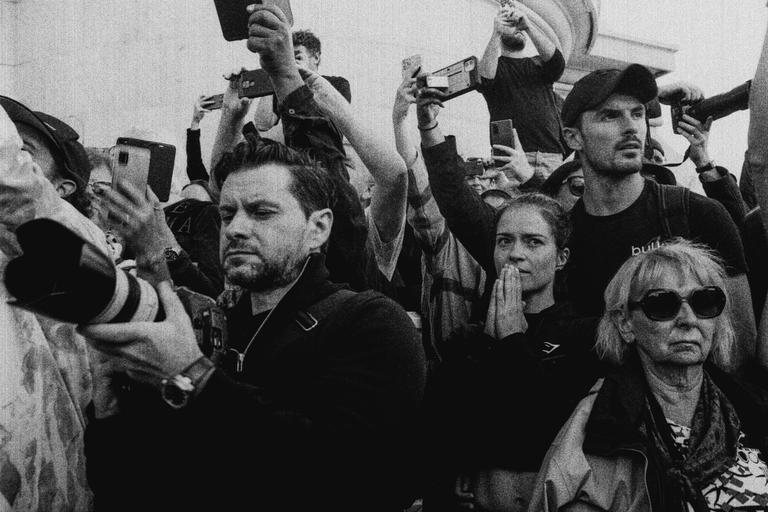 A crowd of people, some holding up phones and cameras, watch an event.