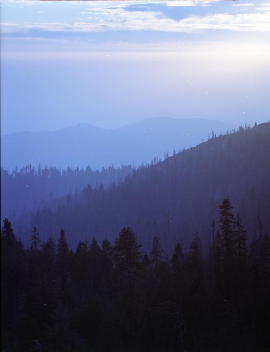 A hazy blue mountain landscape shows layers of forest and hills under a bright sky.