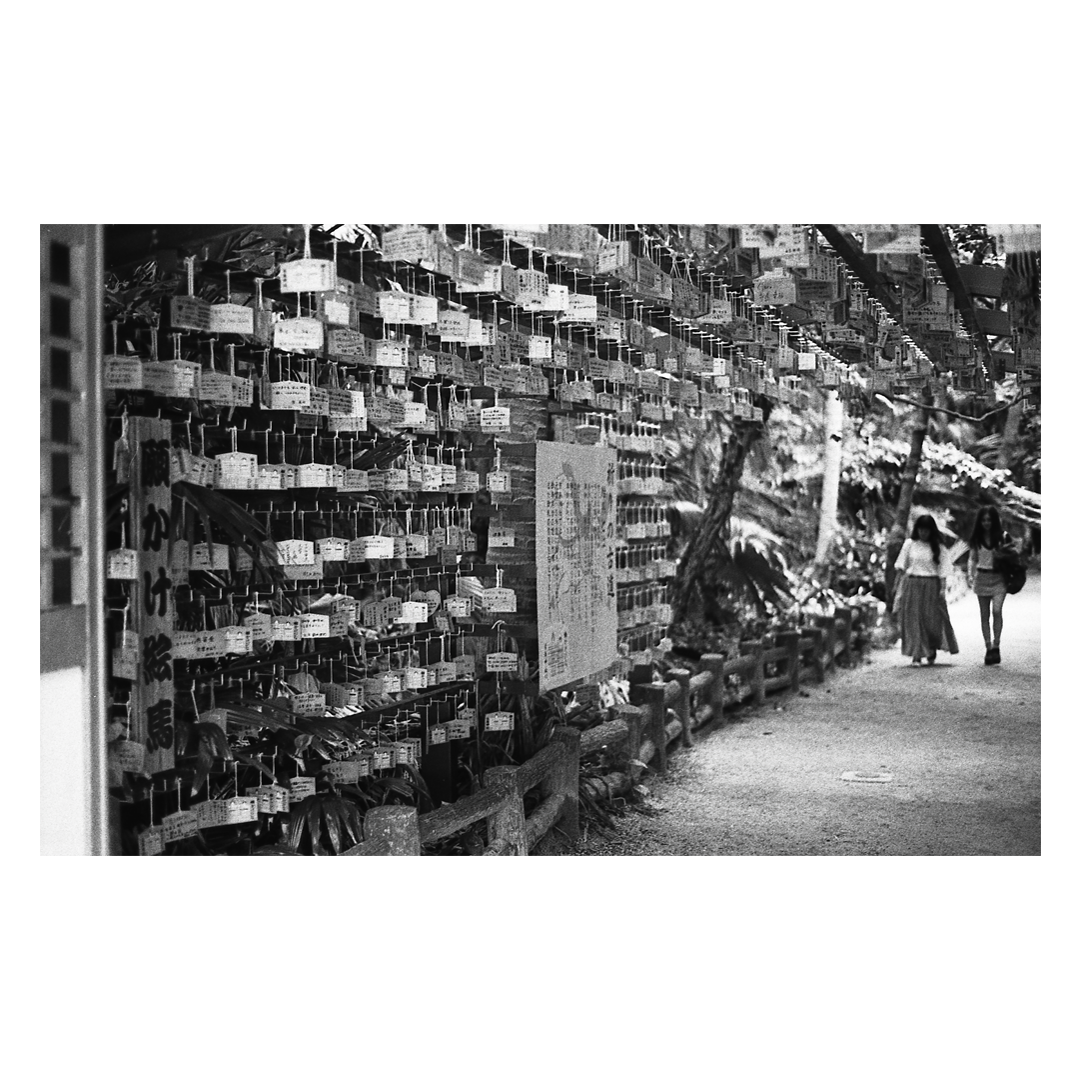 Two women walk past a wall covered in small, hanging wooden plaques.