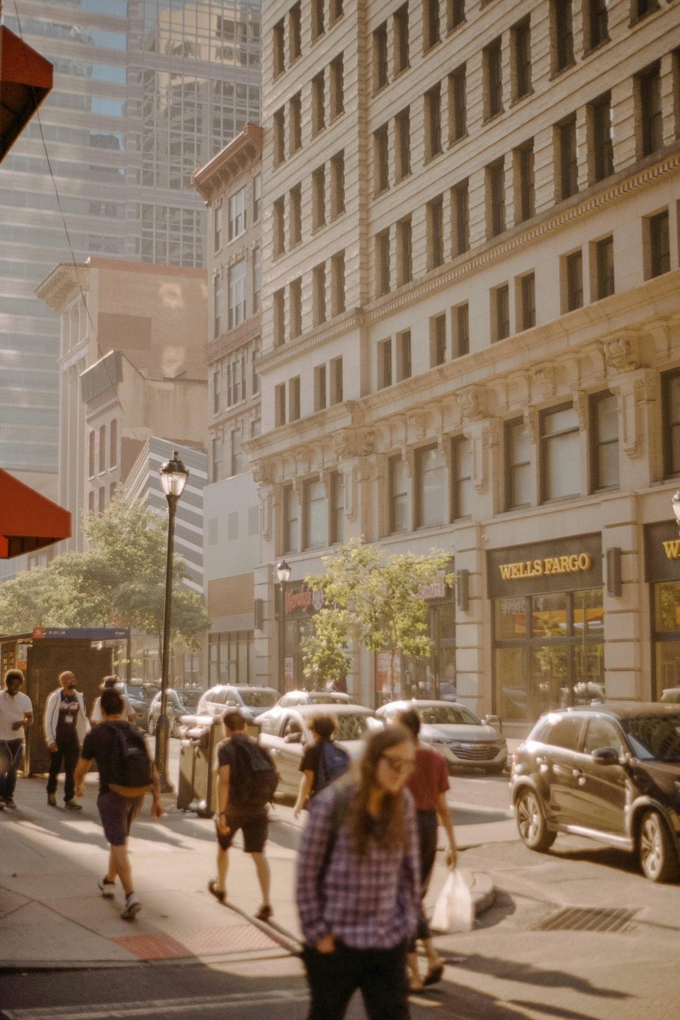 People walk on a city street with tall buildings and cars.