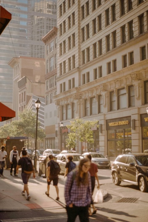 People walk on a city street with tall buildings and cars.