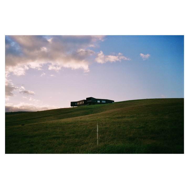 A modern house sits atop a grassy hill under a partly cloudy sky.