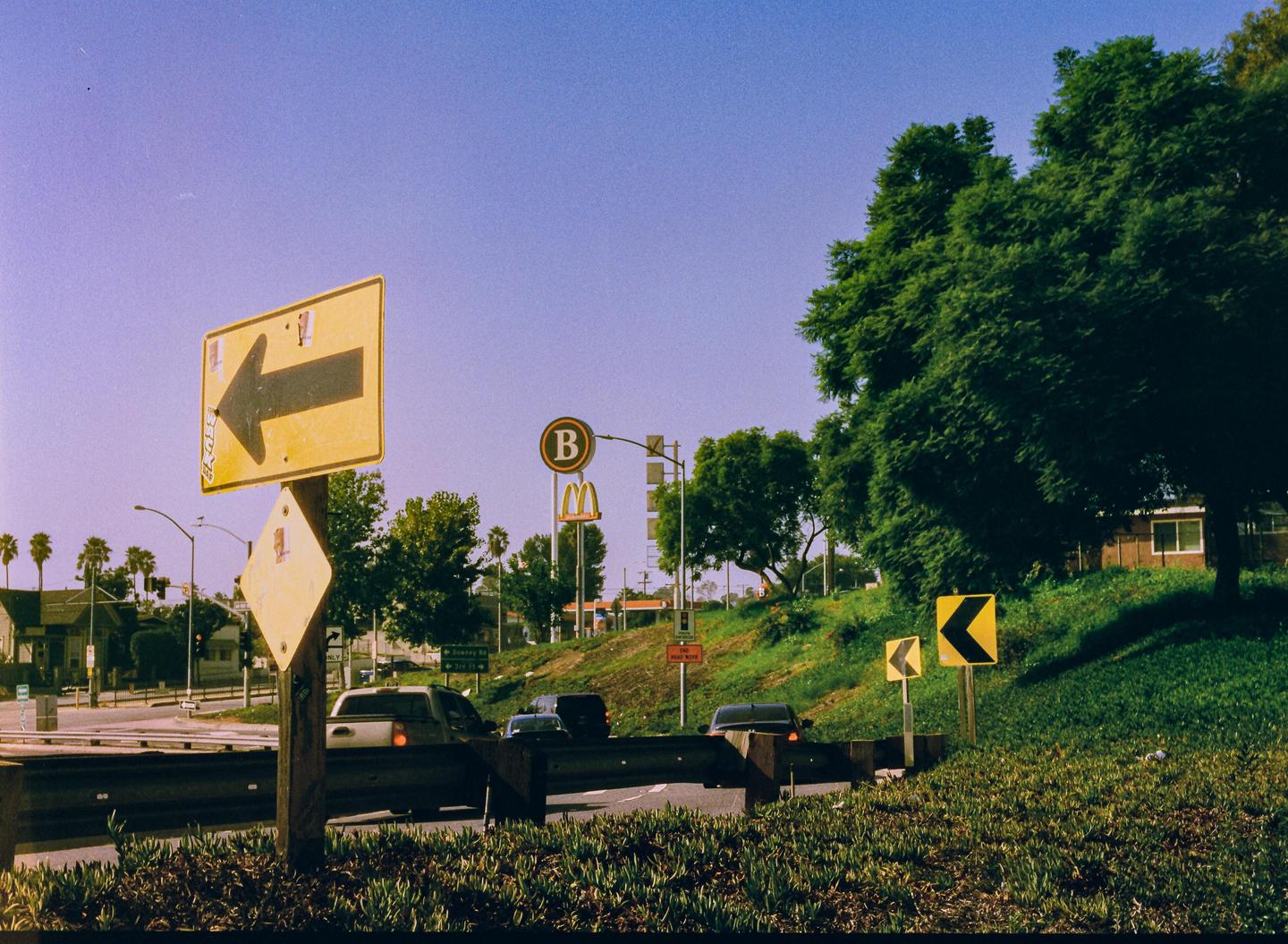 A street scene shows a yellow arrow sign pointing left, with cars on the road and green trees and grass on a hill.