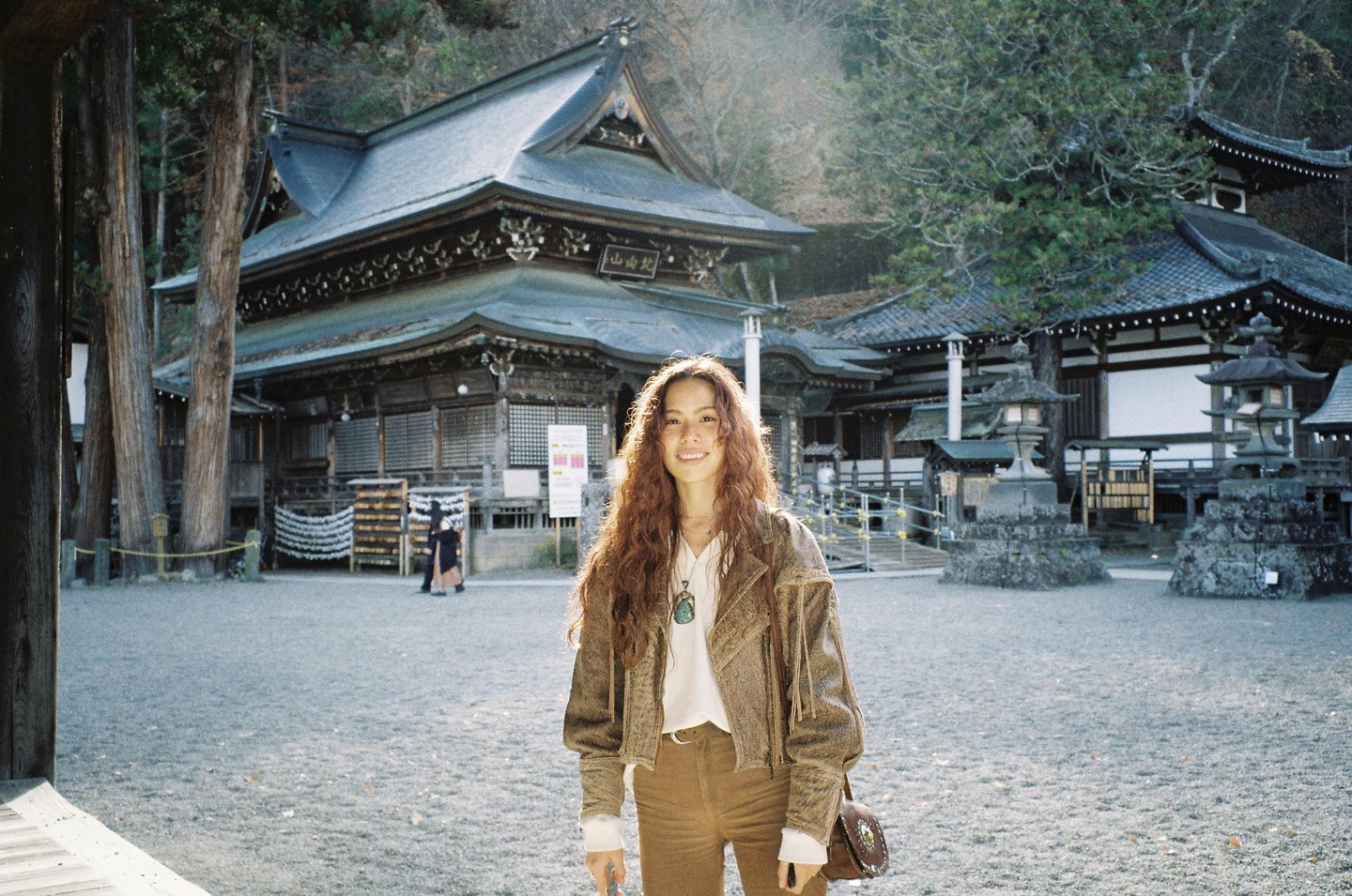 A woman with long, curly hair smiles at the camera in front of a traditional Japanese temple.