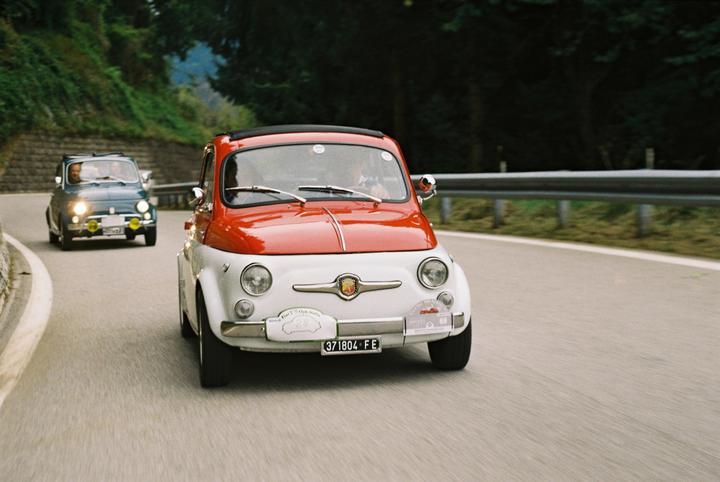 Two Fiat 500 cars drive on a winding road through the alps.