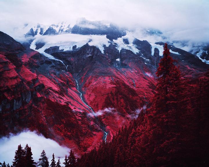 A vibrant red mountain landscape with snow-capped peaks and a stream running through it.