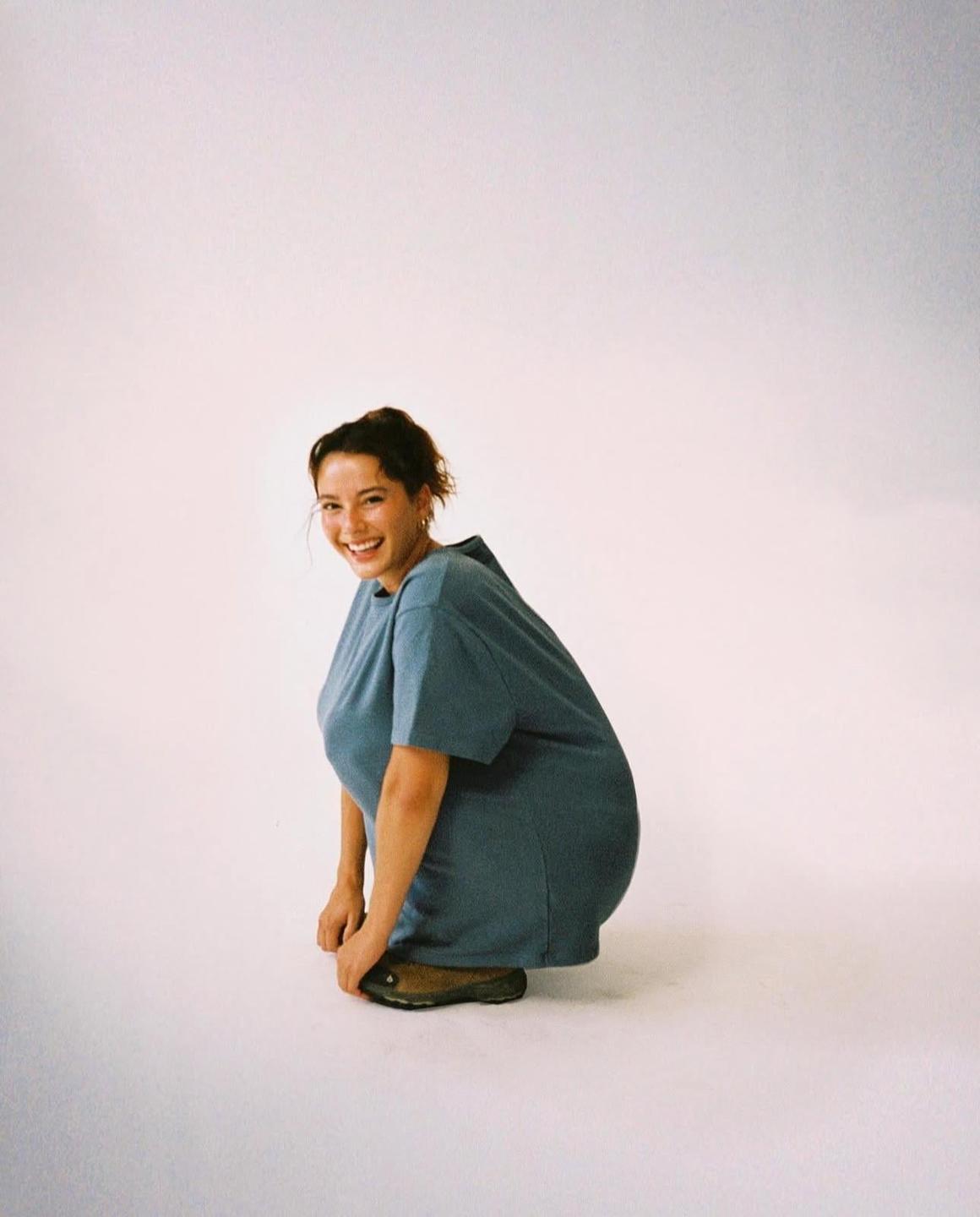 A woman in a blue dress is squatting and smiling at the viewer.