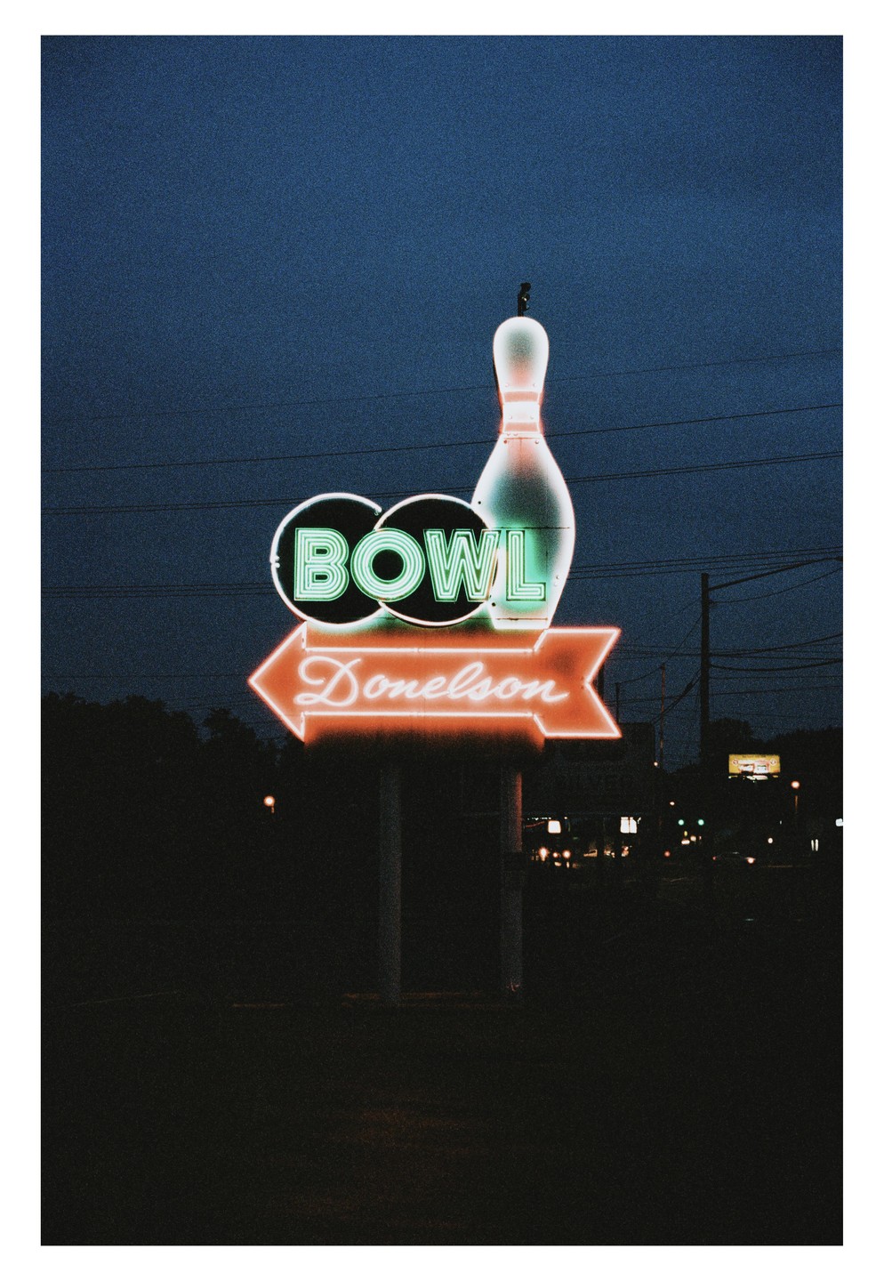 A neon sign for "Donelson Bowl" with a bowling pin is illuminated against a dark blue sky at night.