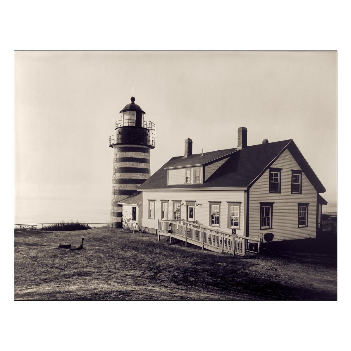 A lighthouse with horizontal stripes stands next to a house with a ramp leading to its entrance.