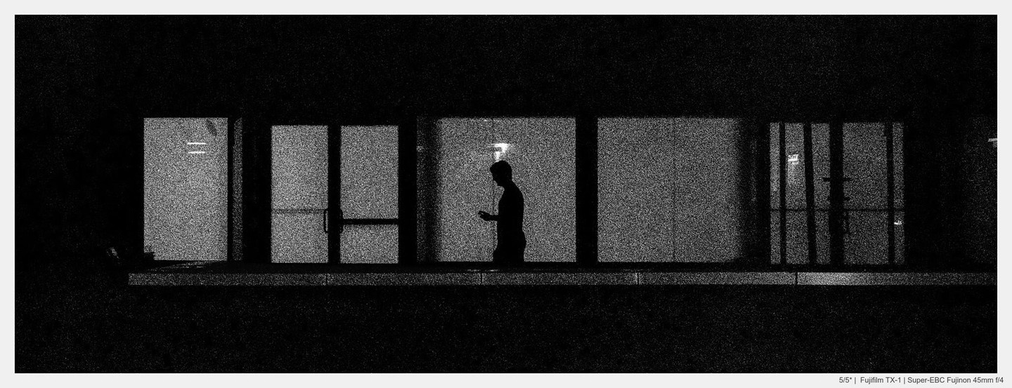 A man stands in silhouette against a brightly lit window, looking at his phone.