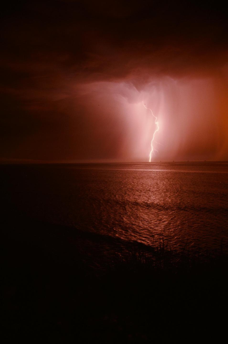 A bolt of lightning strikes the ocean during a storm at night.