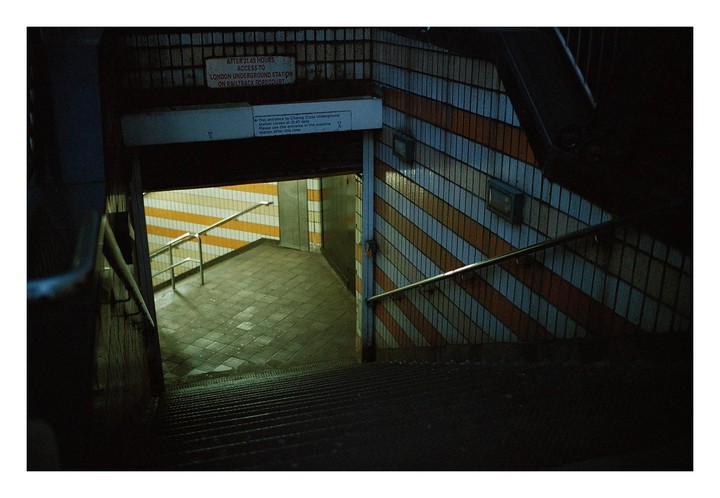 A dark stairwell leads down to a brightly lit underground station with striped walls.