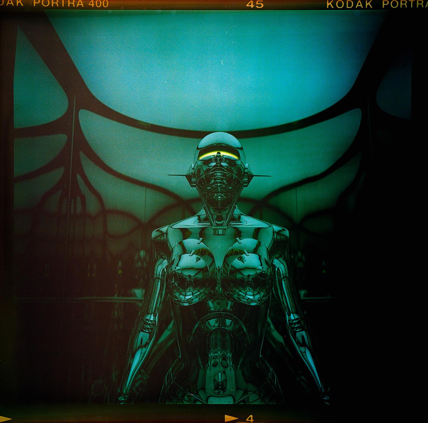 A chrome robot with a glowing yellow visor stands in a dark room with a teal ceiling.