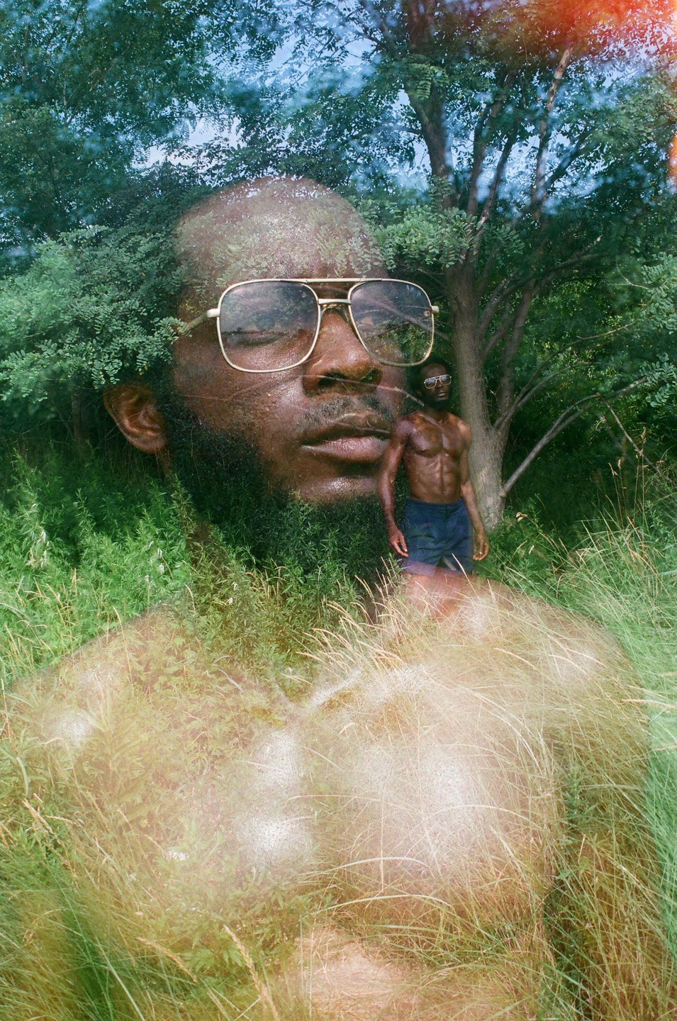 A double exposure shows a man wearing sunglasses with his eyes closed, superimposed over a smaller image of himself standing shirtless in a grassy, wooded area.