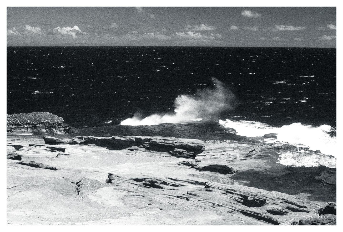 Waves crash against a rocky shore under a cloudy sky.