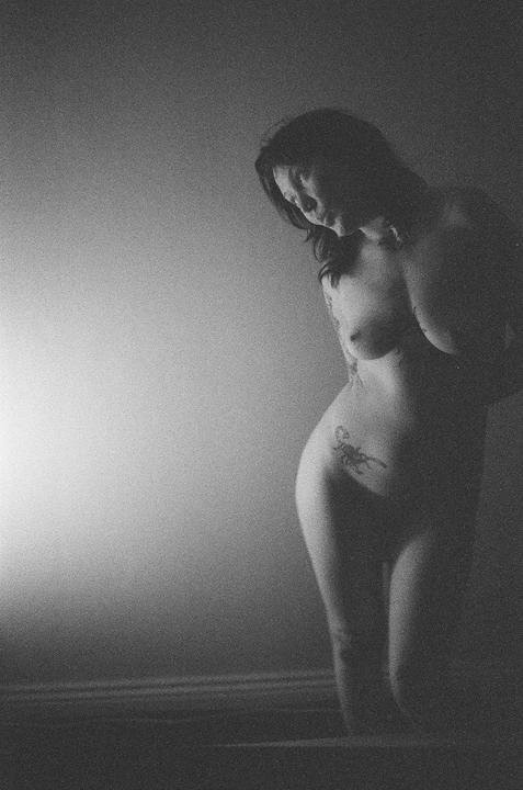 A woman with a scorpion tattoo on her hip is illuminated by a bright light from the left.