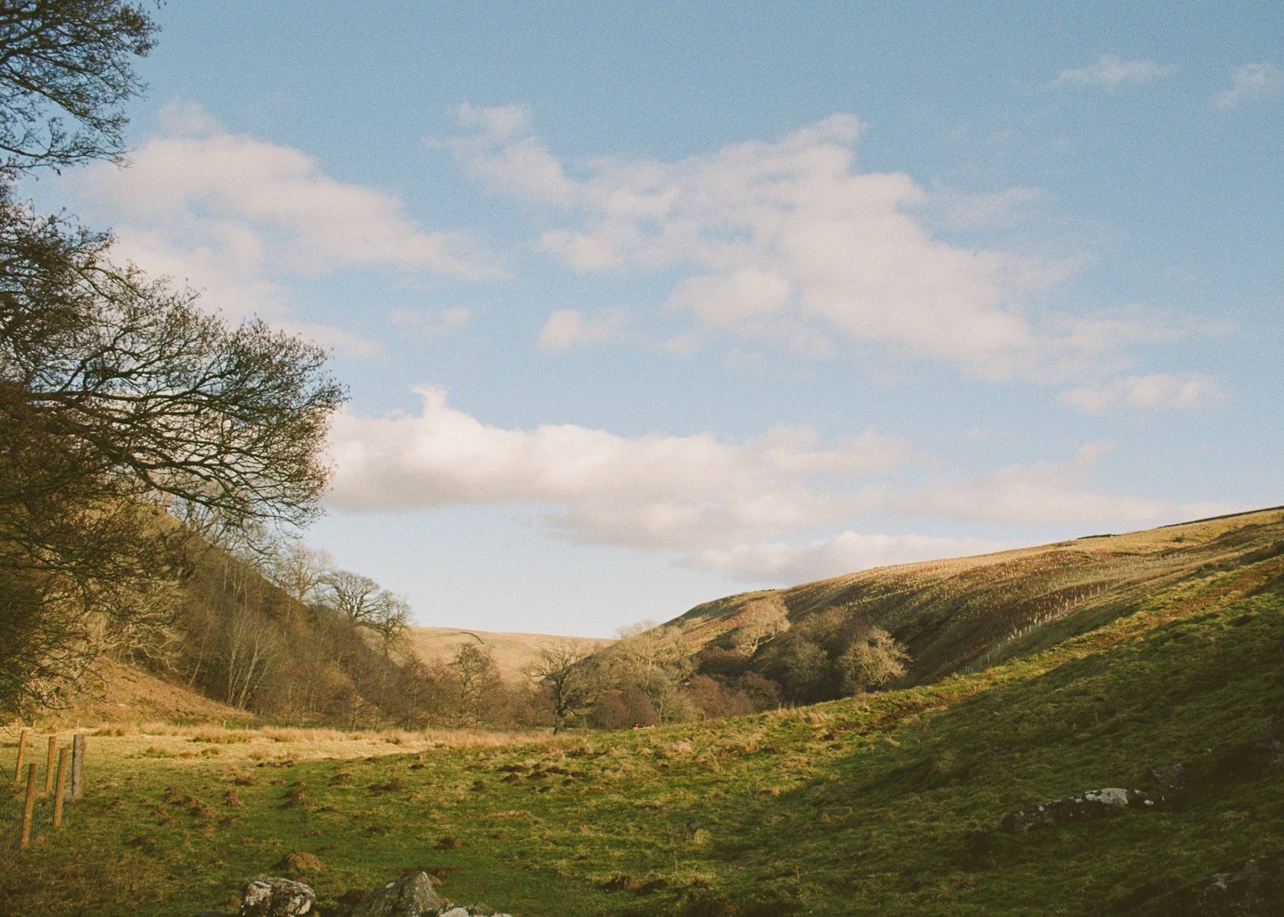 A valley with green and brown hills is visible under a blue sky with white clouds.
