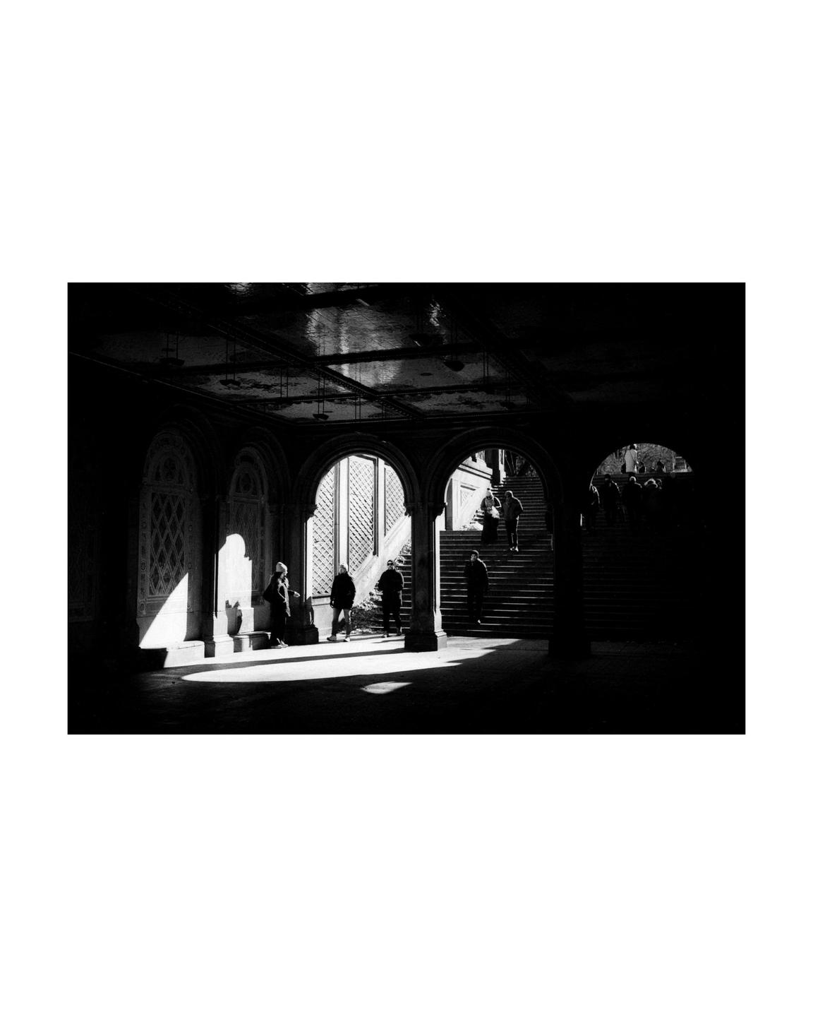 People walk through a dark arched passageway with bright light illuminating parts of the floor and walls.