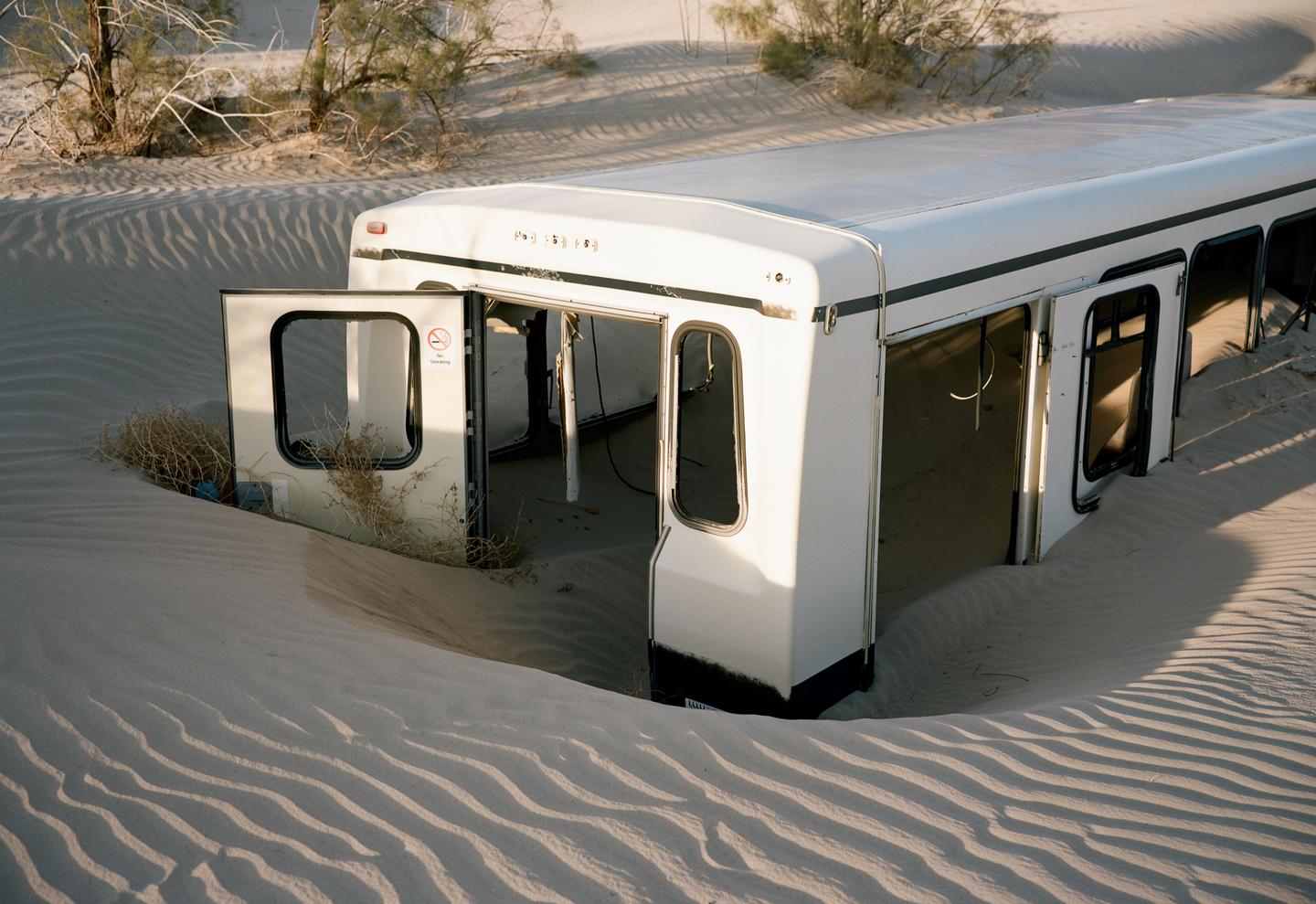 A white vehicle is half-buried in sand dunes with its doors open.