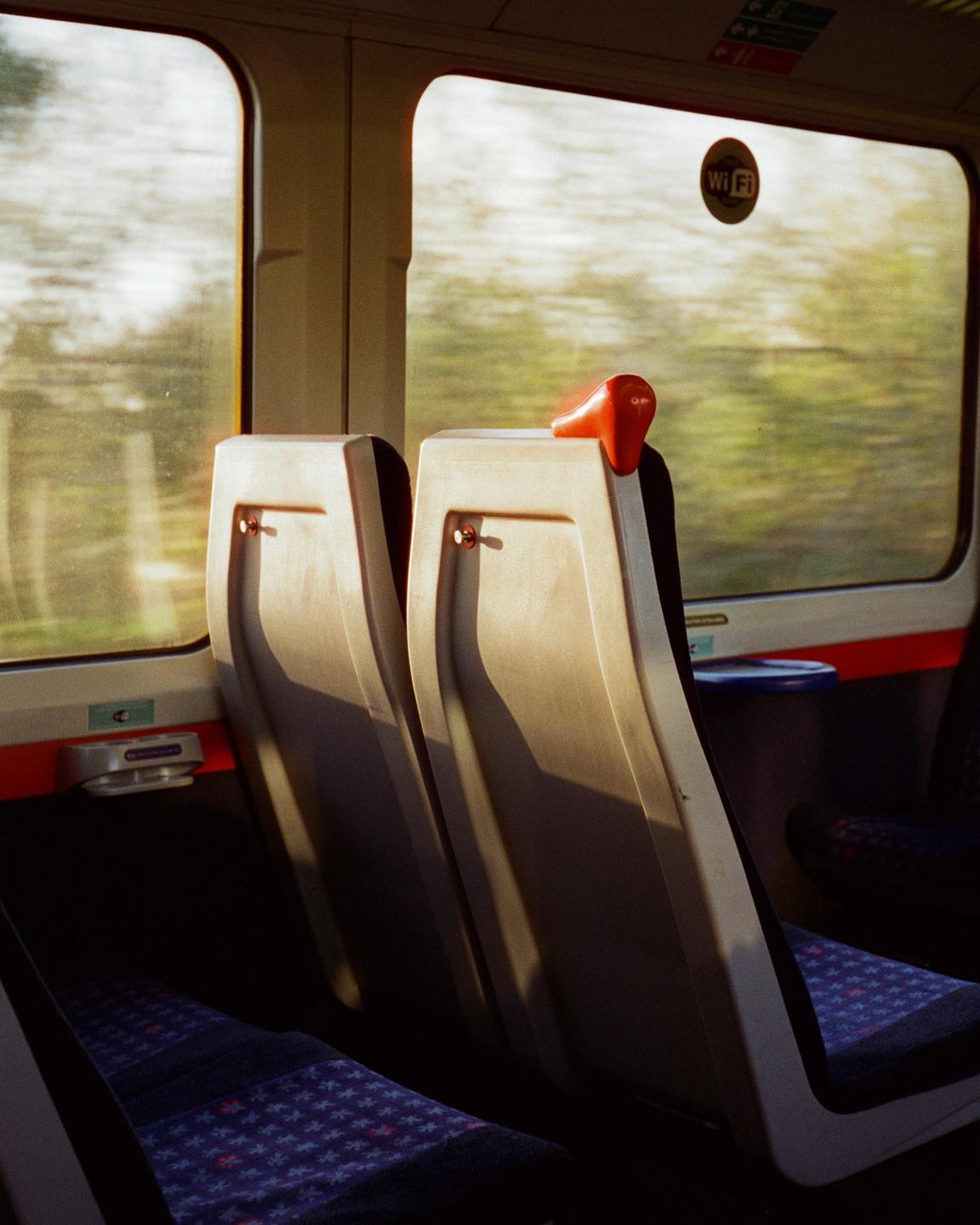Sunlight streams through the window of a moving train, illuminating two empty seats.