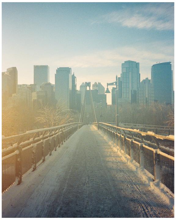 A snow-covered bridge leads towards a city skyline under a hazy sky.