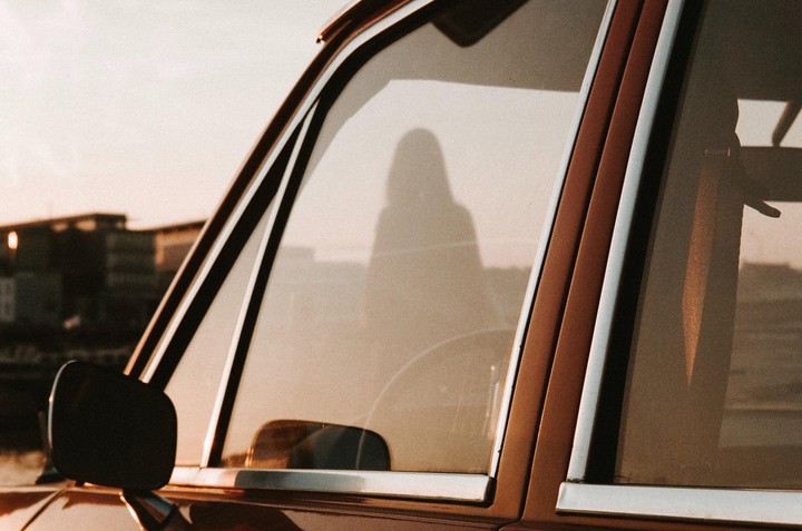 The shadow of a person is visible on the window of a brown car during golden hour.