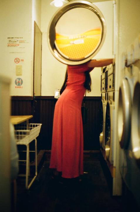 A woman in a red dress leans into a washing machine in a laundromat.
