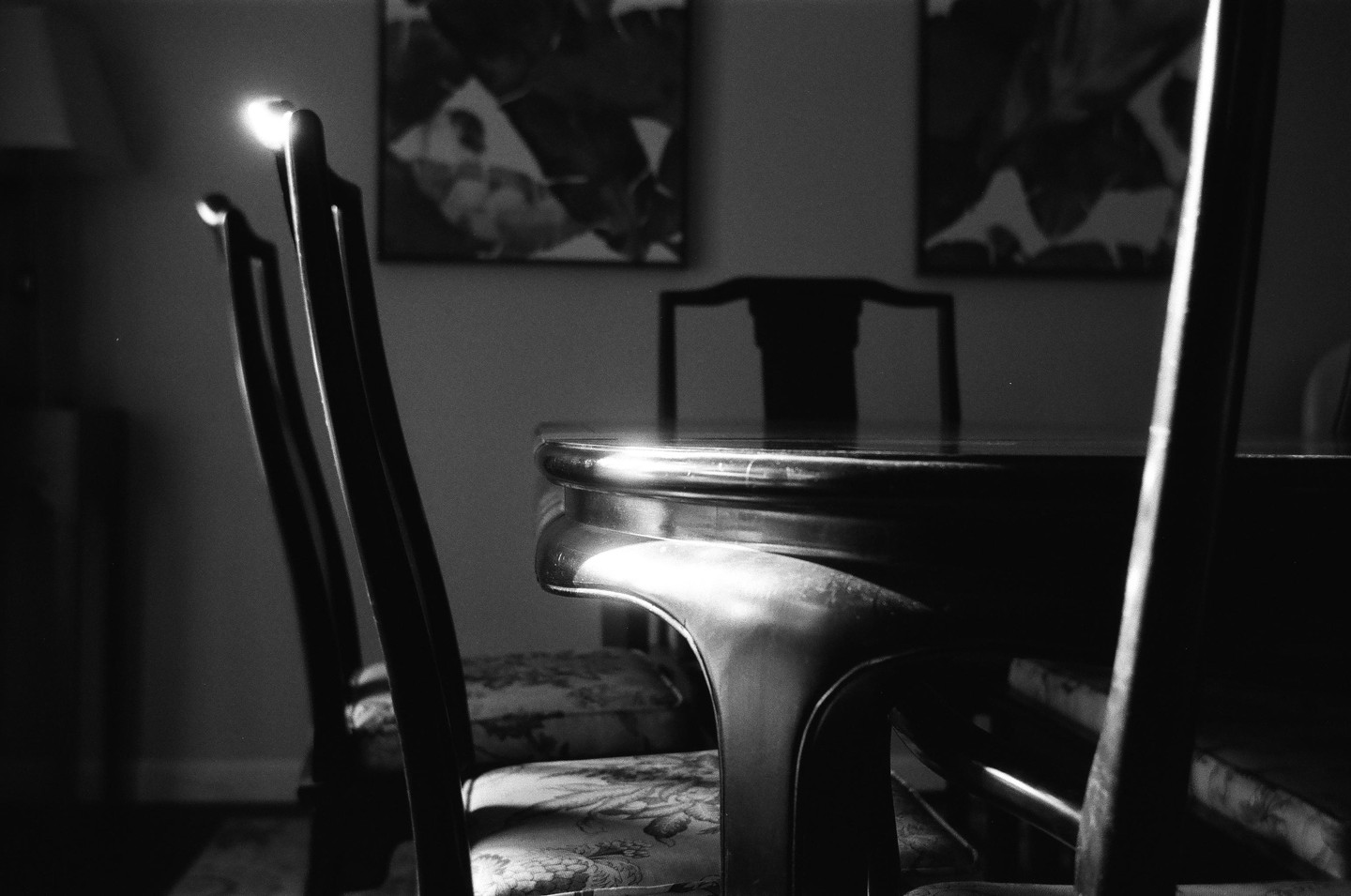 Sunlight illuminates a dining table and chairs in a room with artwork on the wall.