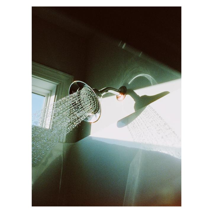 A shower head sprays water into a bathtub, illuminated by a shaft of sunlight.