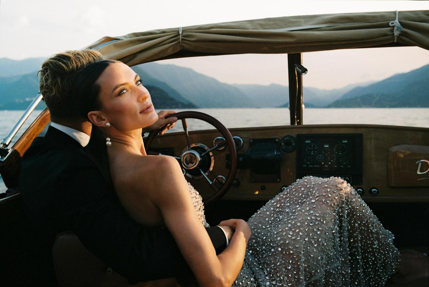 A couple sits in a boat on a lake with mountains in the background.