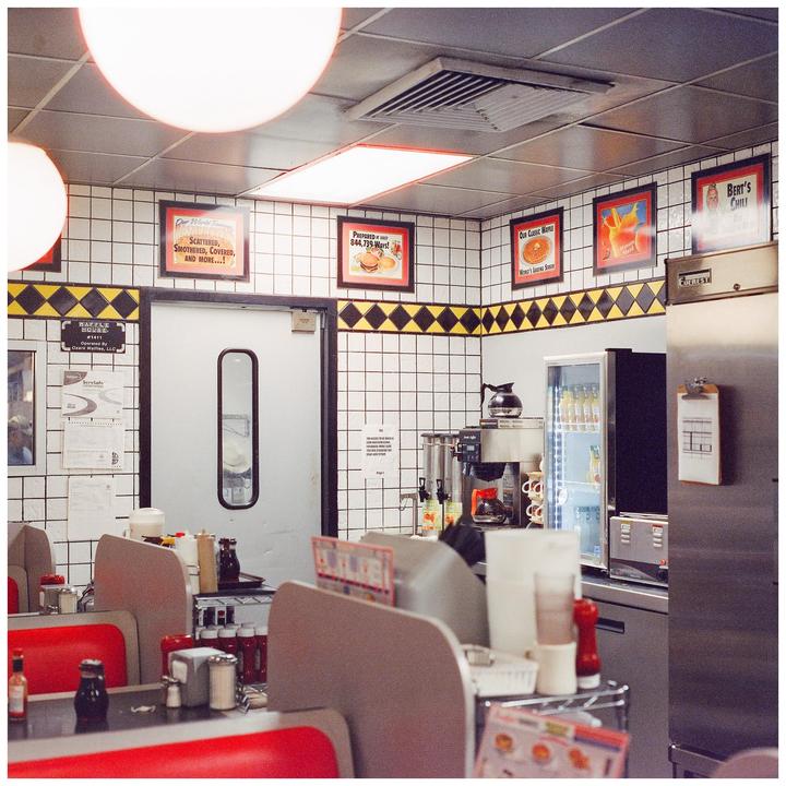 A diner interior features red booths, white tiled walls, and various food advertisements.