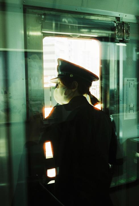 A person in a uniform and a face mask looks out a train window.