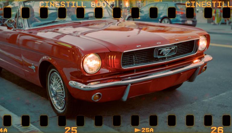 A red convertible car with its headlights on is parked on a street.