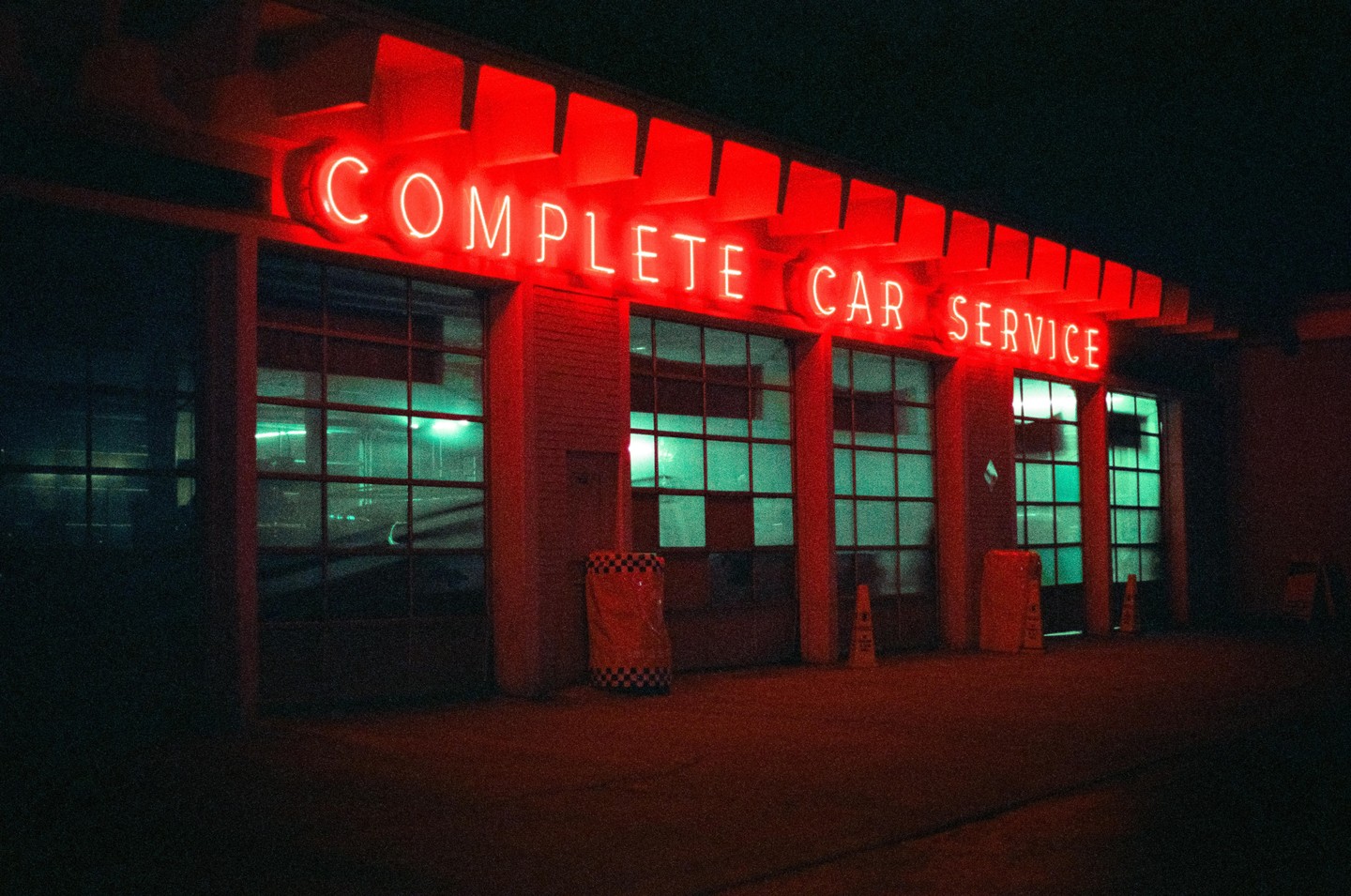 A car service station with a red neon sign that reads "COMPLETE CAR SERVICE" is illuminated at night.