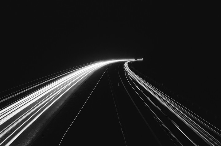 Light trails from vehicles illuminate a dark, curving highway at night.