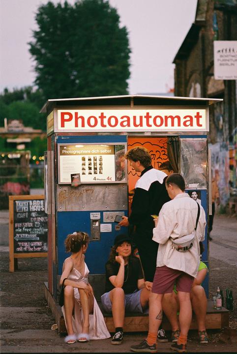 A group of people are gathered around a photo booth on a street.