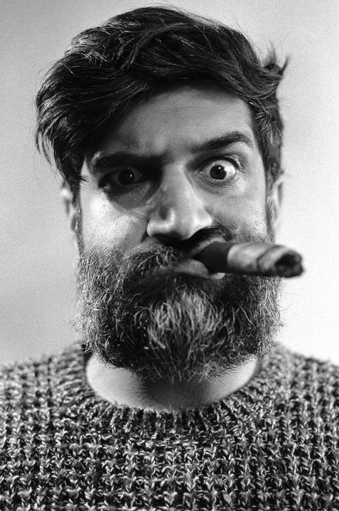 A man with a beard and a cigar in his mouth stares wide-eyed at the viewer.