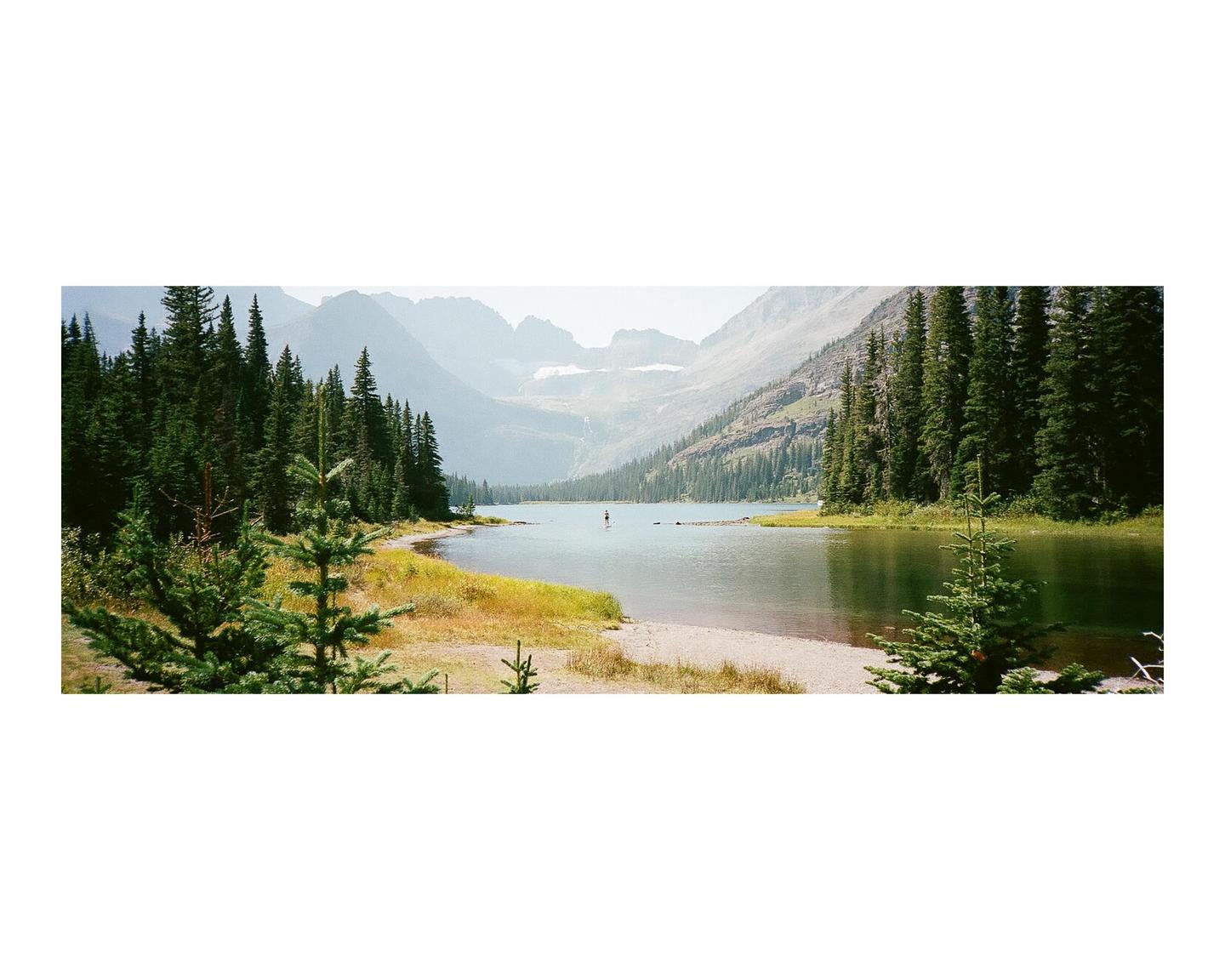A person paddleboards on a lake surrounded by a forest and mountains.