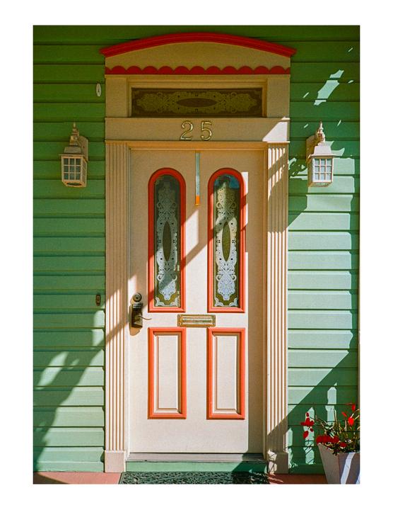 A white door with red trim and the number 25 is set into a green wooden wall.