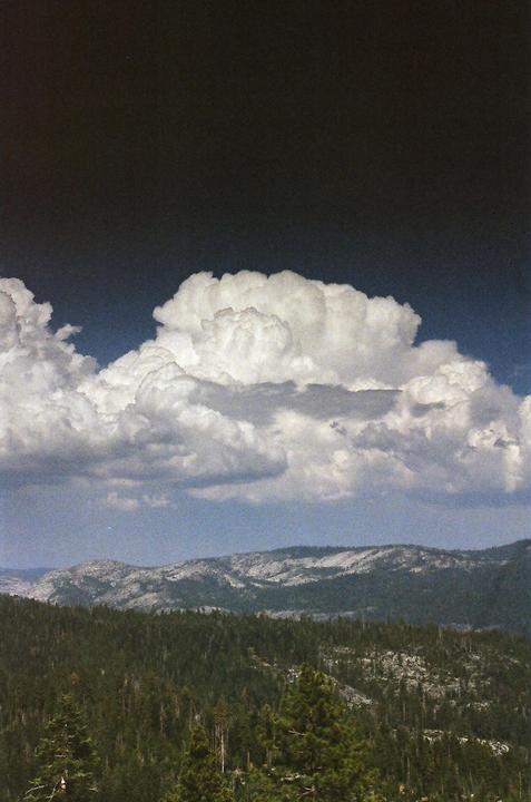 A large, dark cloud formation looms over a forest and mountain range.